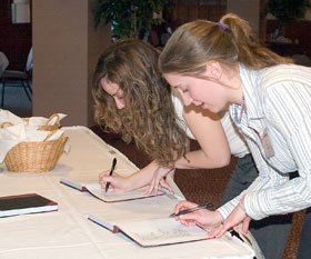 Freshmen Nicole Millar, foreground, and Julie Molina sign the chapter roll book at the induction ceremony for Alpha Lambda Delta on March 27.