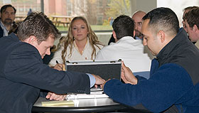 Two tax evasion suspects portrayed by IRS agents Jason Ryan, left, and Ken Clark make a mock transaction. Student investigator Katherine Antonitis, a senior majoring in accounting, performs surveillance.