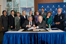 Chancellor Marc Herzog, seated left, and President Michael J. Hogan sign an articulation agreement between the community colleges and UConn, as state legislators and representatives of the community college system look on. 