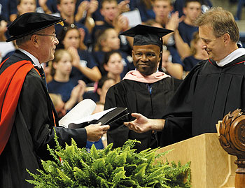 Provost Peter J. Nicholls, left, receives a list of new students from M. Dolan Evanovich, right, vice president of enrollment management, planning, and institutional research, during Convocation, as Lee Melvin, director of undergraduate admissions, looks on.