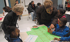 Professor M. Katherine Gavin, left, listens as eight-year-old William Amaro explains a math game to his mother, Prescilla Amaro, during family night at a math enrichment club at Hartford’s Breakthrough Magnet School. Gavin leads a research team that developed the curriculum used by the after-school club.